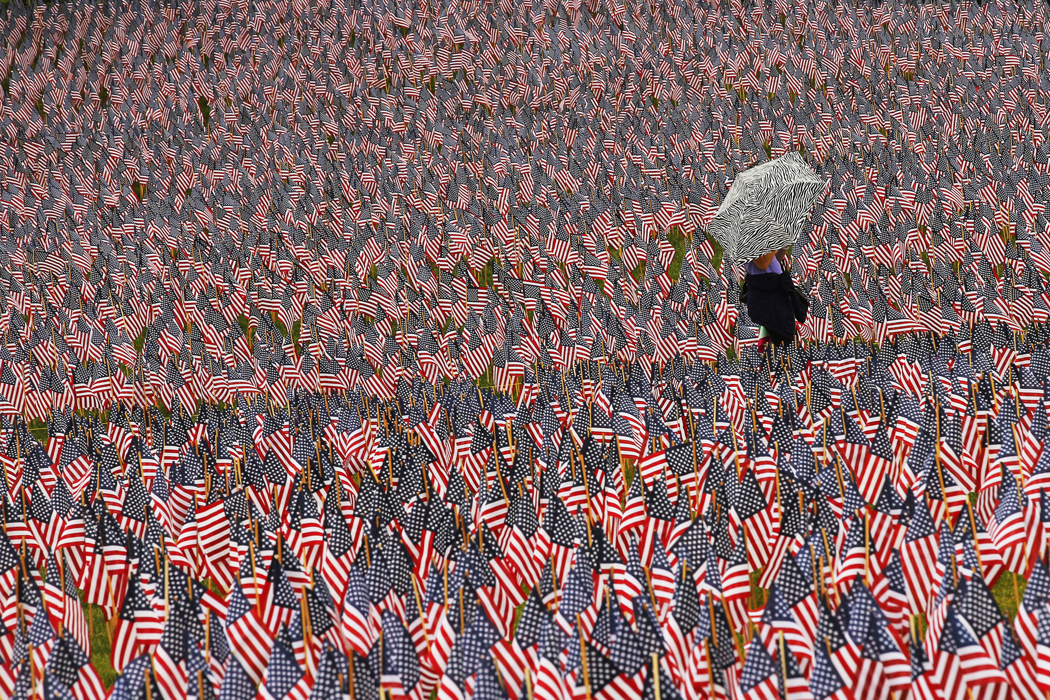 Pedestrian carrying an umbrella walks through a Memorial Day display of United States flags on the Boston Common in Boston