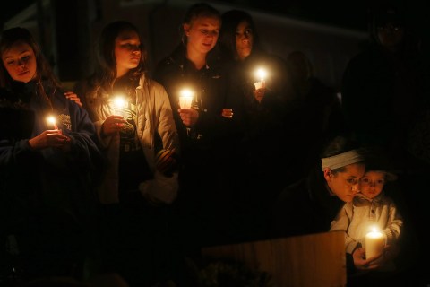 image: mourners hold candles at a memorial for victims on the first Sunday following the mass shooting at Sandy Hook Elementary