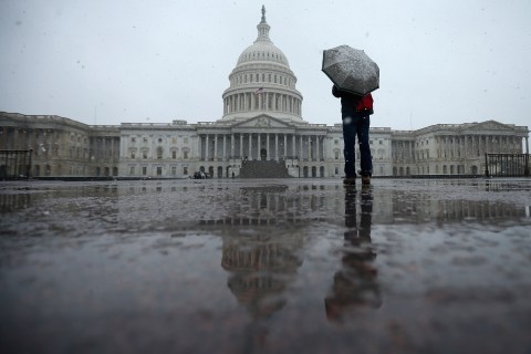 A tourist takes cover underneath an umbrella while snapping a photo of the U.S. Capitol as snow and rain falls in Washington