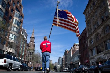 Lt. Mike Murphy of the Newton, Mass., fire dept., carries an American flag down the middle of Boylston Street after observing a moment of silence in honor of the victims of the bombing at the Boston Marathon near the race finish line, Monday, April 22, 2013, in Boston, Mass.