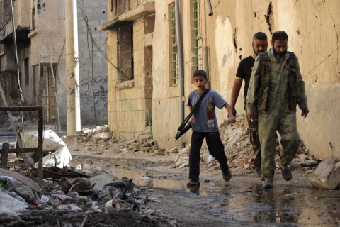A boy carries a weapon as he walks with members of the Free Syrian Army on a damaged street filled with debris in Deir al-Zor