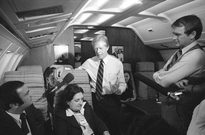 President Jimmy Carter and press secretary Jody Powell, right, chat with Helen Thomas, center, while standing in the aisle of Air Force One prior to landing at Andrews Air Force Base, Md., Oct. 20, 1979. 
