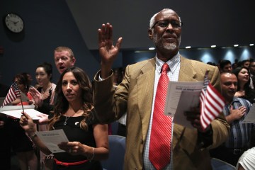 Carolina Hall (2nd R) of Annandale, Virginia, who was originally from Colombia; Ahmed Ali Abokor (R) of Annandale, Virginia, who was originally from Somalia; and other candidates recite the Pledge of Allegiance during a naturalization ceremony August 13, 2013 at Woodson High School in Fairfax, Virginia. (Photo by Alex Wong/Getty Images)