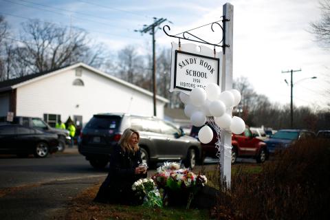 A woman places flowers at a memorial near a sign for Sandy Hook Elementary School 